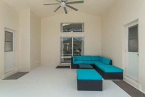 A room with a ceiling fan, a sliding glass door leading to a balcony, and a sectional sofa with cushions. - 5-Bed Villa w/ Private Pool (Davenport)