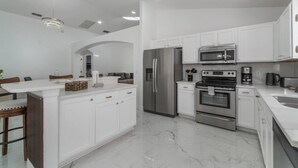 Eine moderne Küche mit weißen Schränken, einem Edelstahlkühlschrank, einem Backofen und einer Mikrowelle.