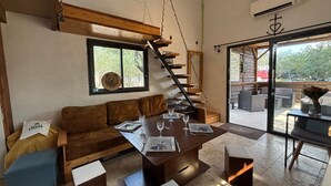 Ein modernes Interieur mit einer Holztreppe, einem Essbereich mit Tisch für vier Personen und einem großen Fenster mit Blick ins Freie.