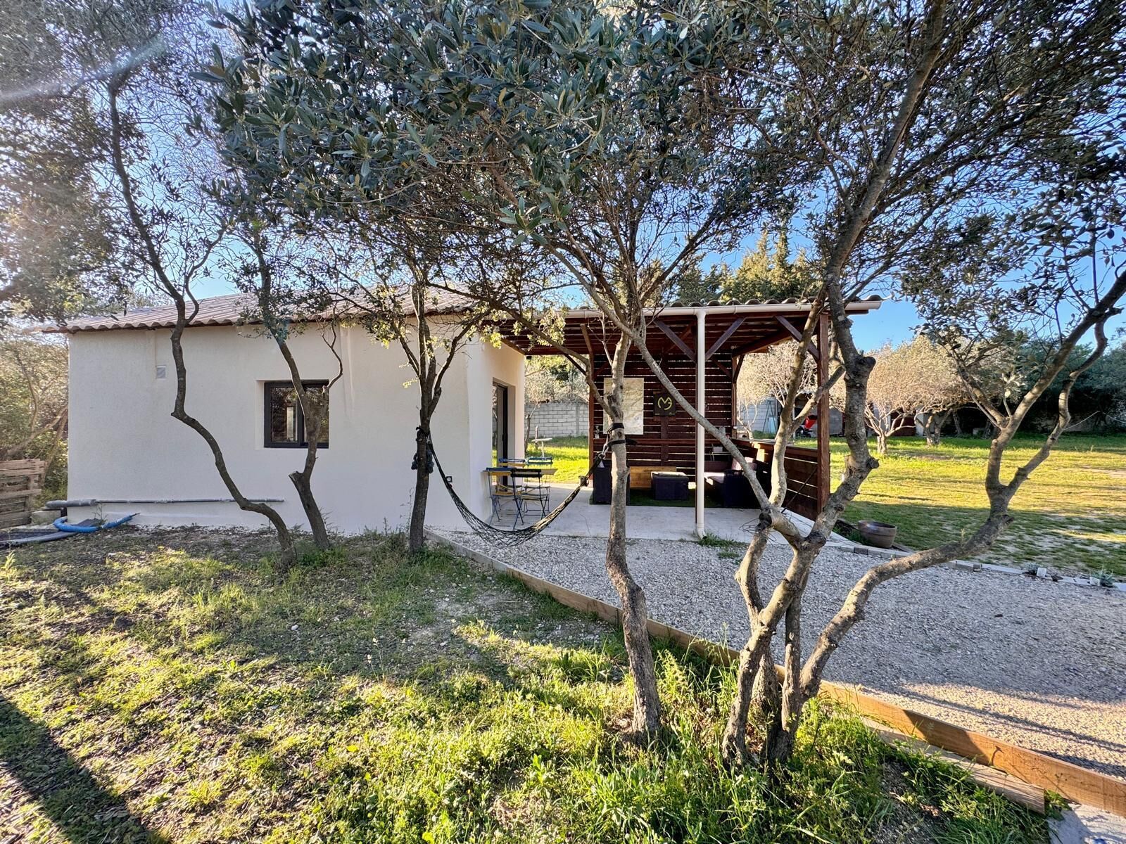 Ein Haus mit Terrasse, kleinem Garten und einer Pergola.