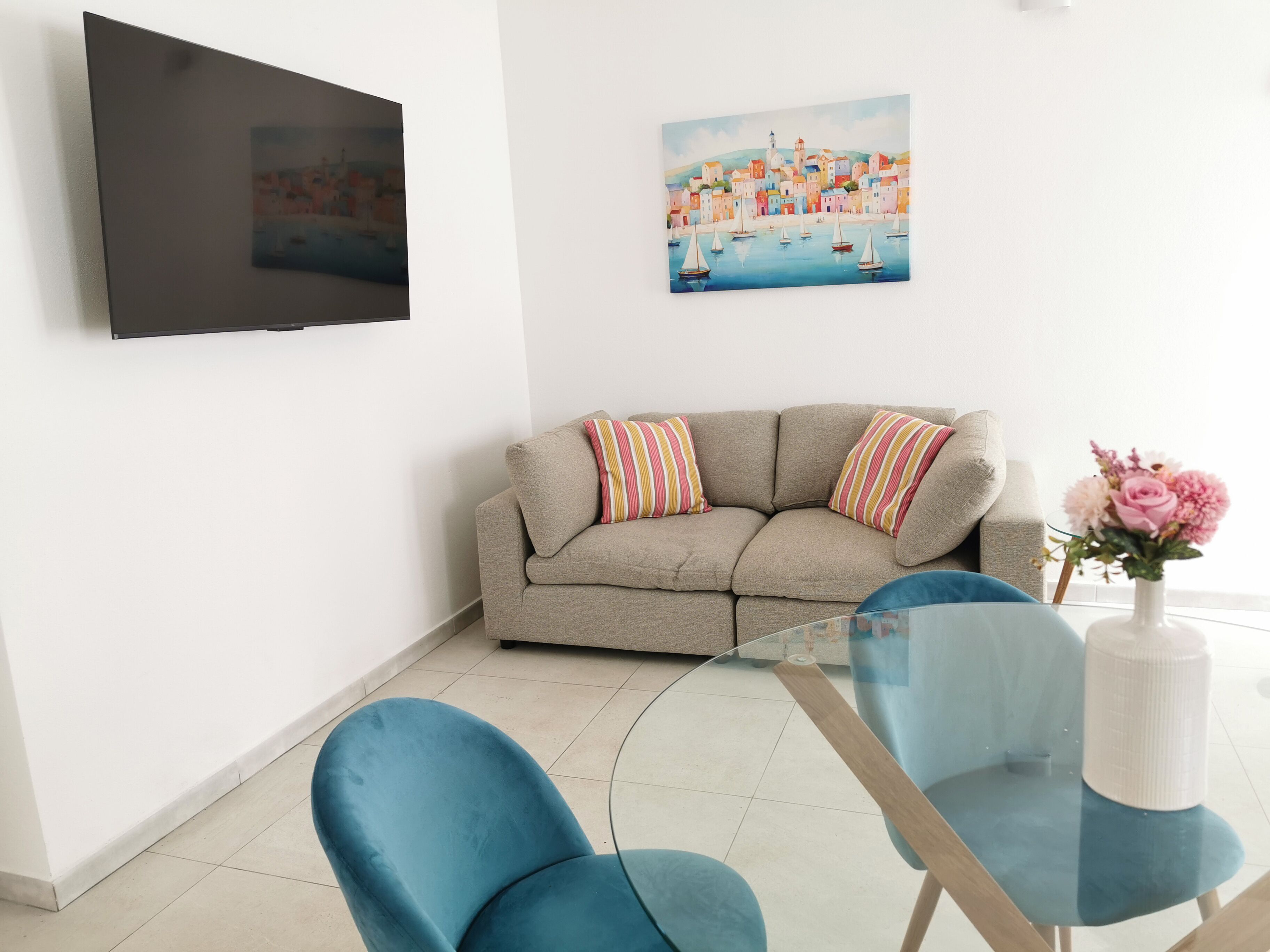 A living room with a sofa, a TV mounted on the wall, and a painting above the sofa.