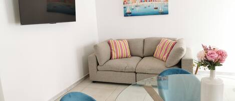 A living room with a sofa, a TV mounted on the wall, and a painting above the sofa.