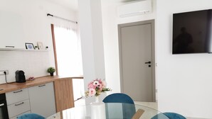 Eine moderne Küche mit Kaffeemaschine, Blumen in einer Vase und einem Essbereich mit Glastisch und blauen Stühlen.