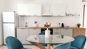 Eine moderne Küche mit weißen Schränken, einem runden Glastisch und blauen Stühlen.