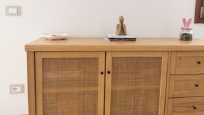 Ein Holzschrank mit Geflechtfront, eine weiße Schüssel, ein Bücherstapel und ein kleines Glas mit Hasen-Deckel.