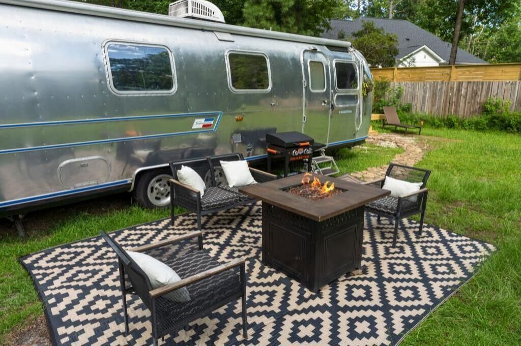 A stationary trailer with a fire pit, outdoor furniture, and a patterned rug.