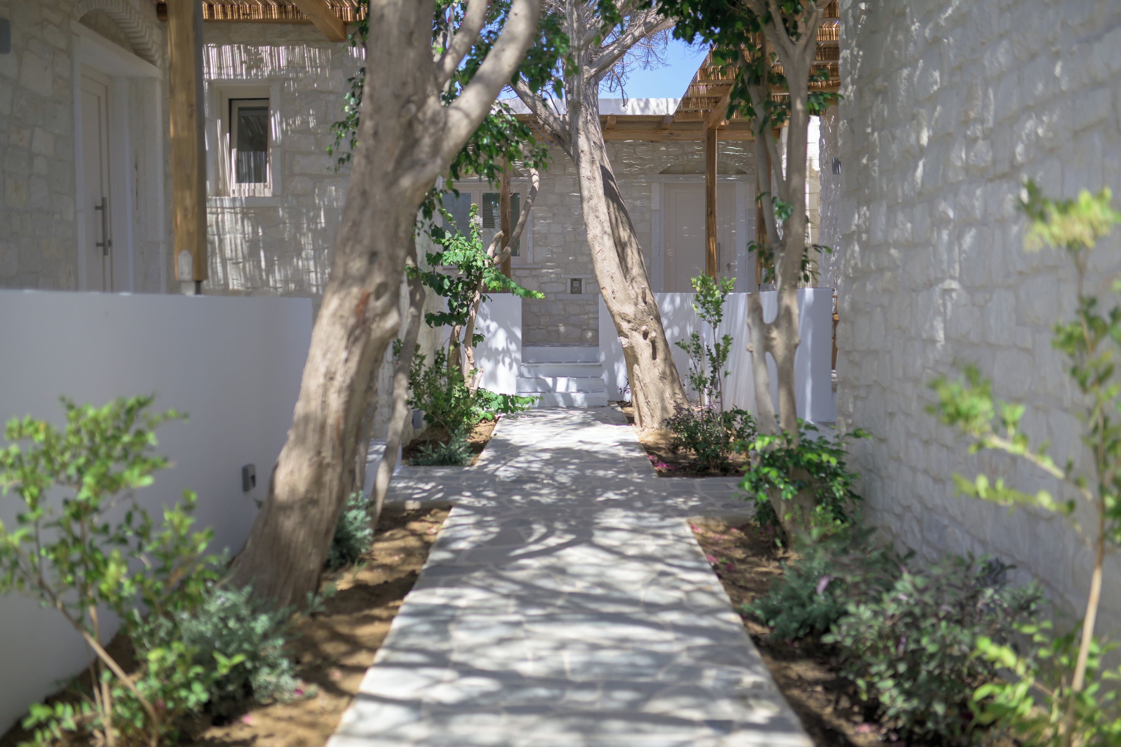 A narrow pathway flanked by stone walls and trees, leading to a building with a wooden balcony.