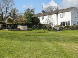 A white house with a stone wall, a hot tub, and a well-maintained lawn.