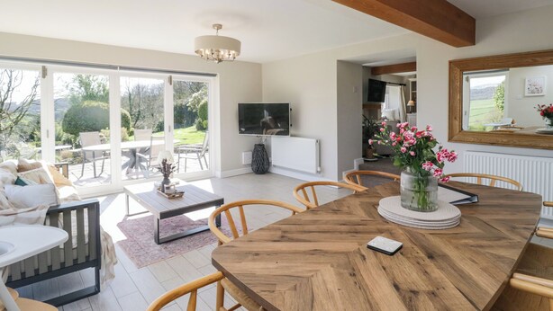 Un amplio salón con una gran mesa de comedor de madera, asientos cómodos, un televisor y vistas al exterior.