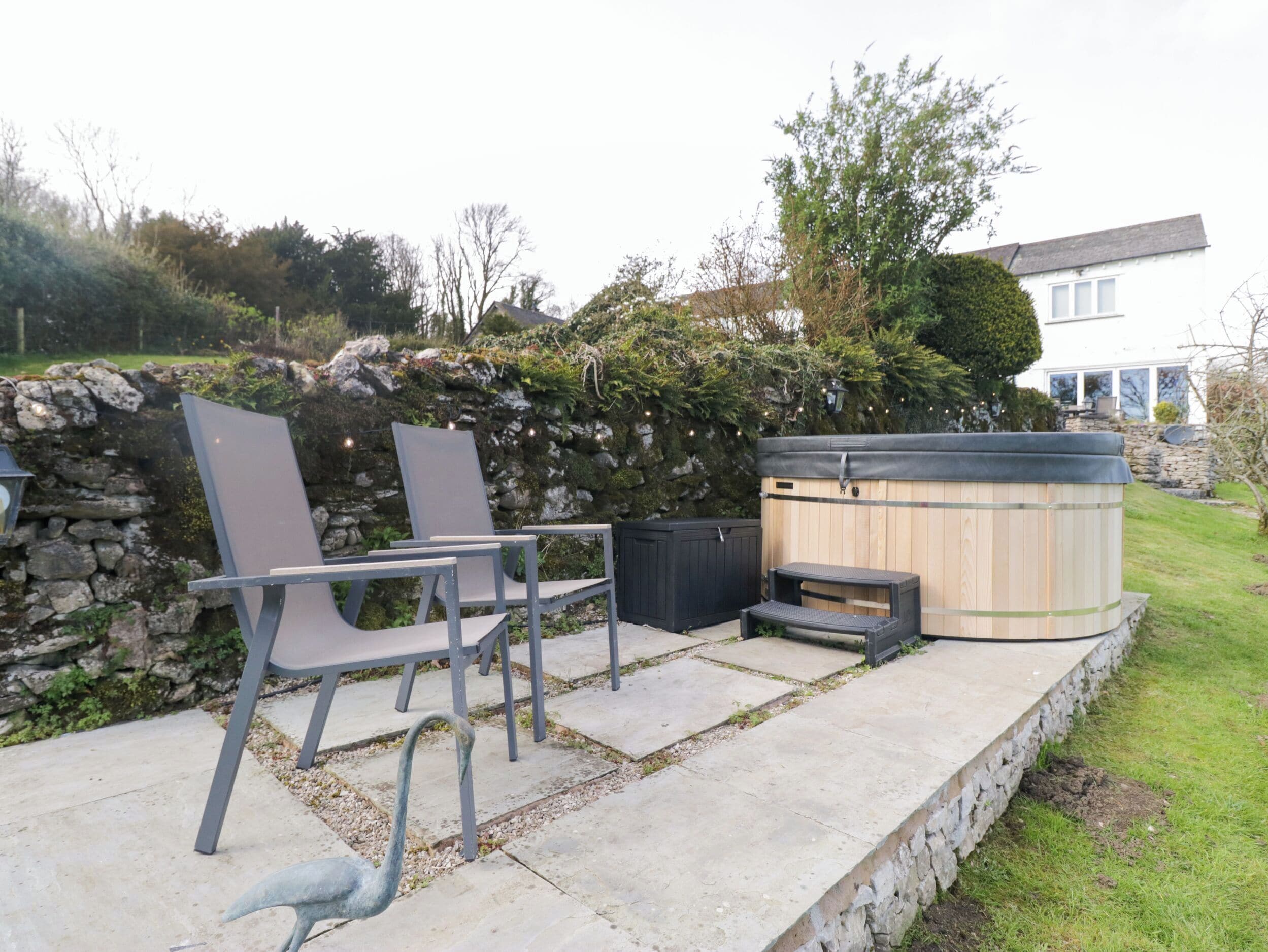 A patio with two chairs, a hot tub, and a stone wall.