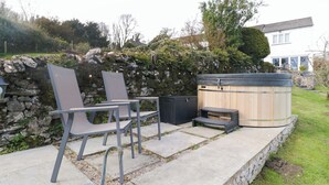 A patio with two chairs, a hot tub, and a stone wall. - Barn Howe (Kendal)
