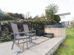 A patio with two chairs, a hot tub, and a stone wall.