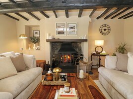 A cozy living room with a fireplace, two sofas, a coffee table with books and candles, and a clock on the wall.