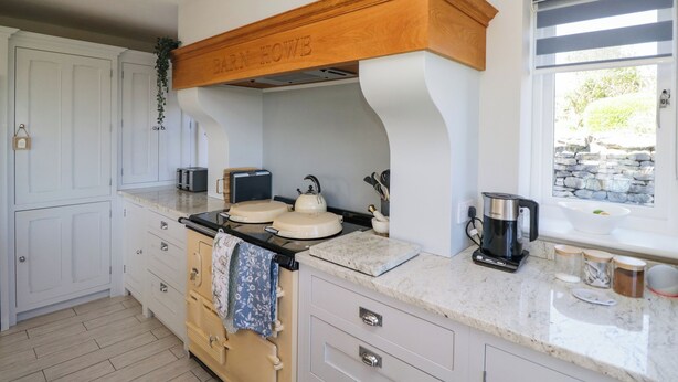 A kitchen with white cabinetry, a wooden countertop, a stove, and a window with a stone wall view. - Barn Howe (Kendal)