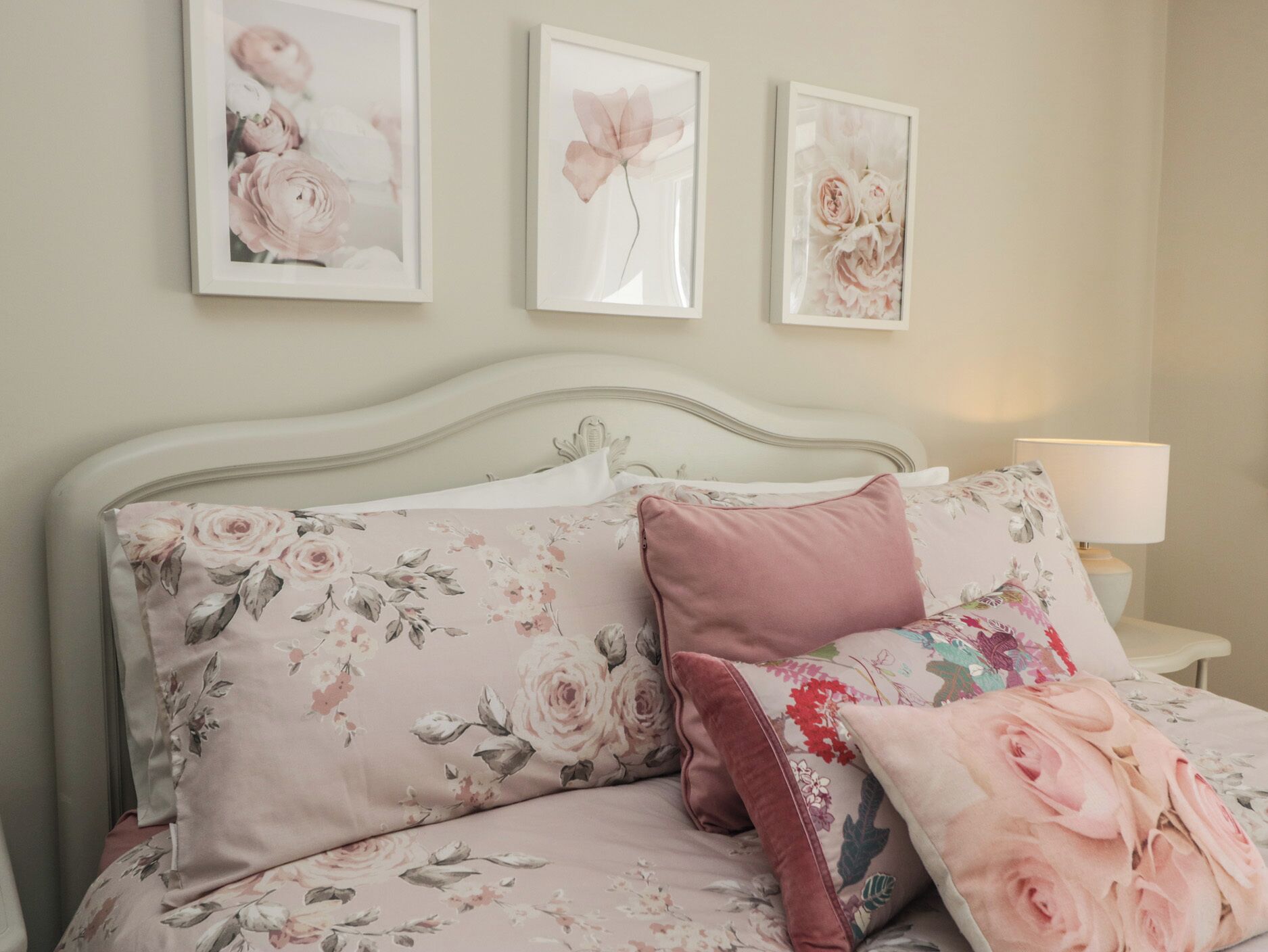 A bed with floral bedding, a headboard, and three framed floral artworks on the wall.