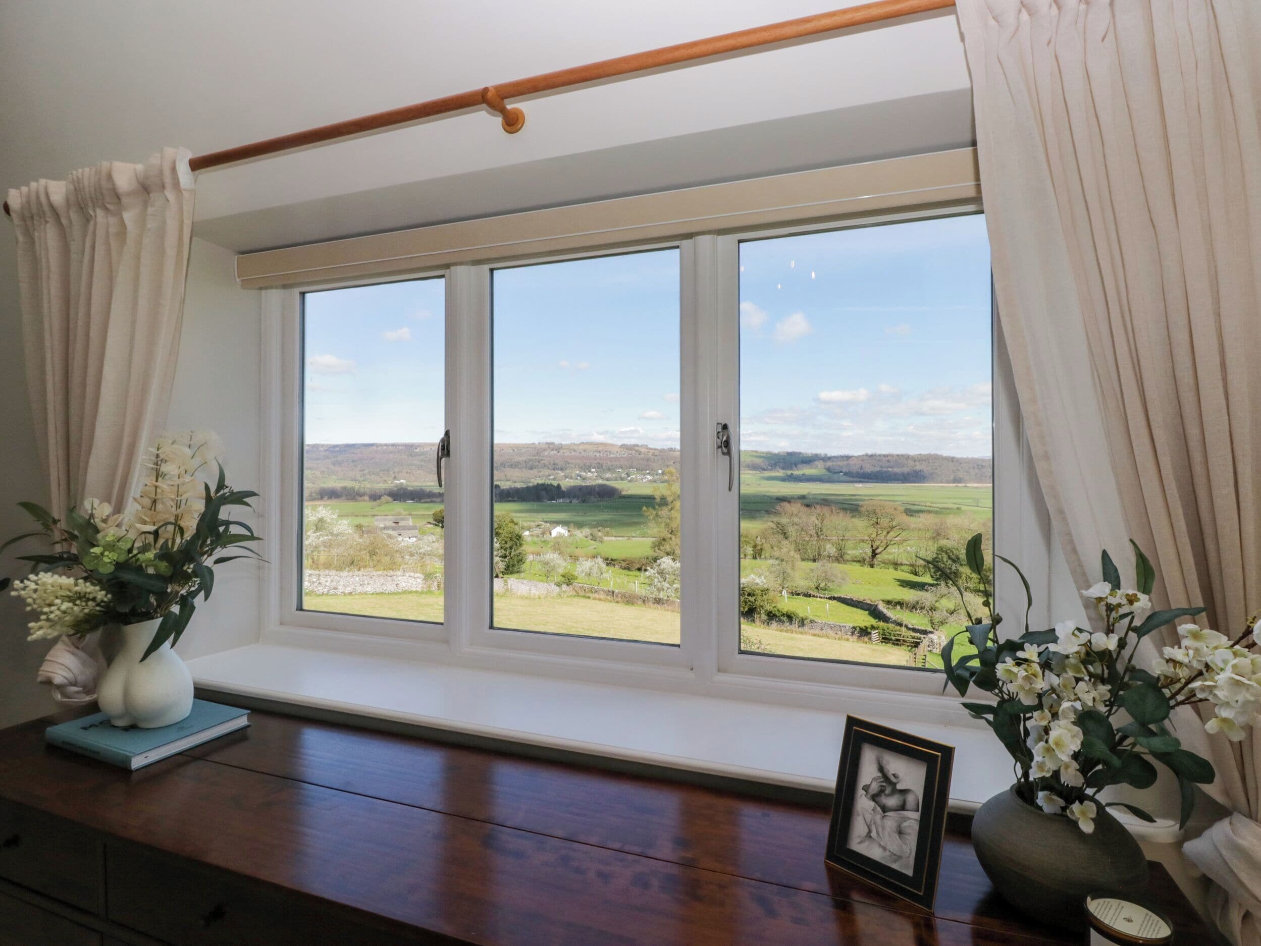 A room with a large window, a wooden floor, and a view of a green landscape.