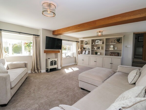 A living room with a sofa, a television, a fireplace, a bookshelf, and a window with curtains. - Barn Howe (Kendal)