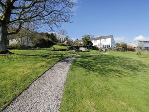 A gravel path leading to a white house with a garden and a greenhouse. - Barn Howe (Kendal)
