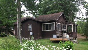 A rustic cabin with a porch, surrounded by a garden with white flowers. - Tamar Vacations (Temagami)