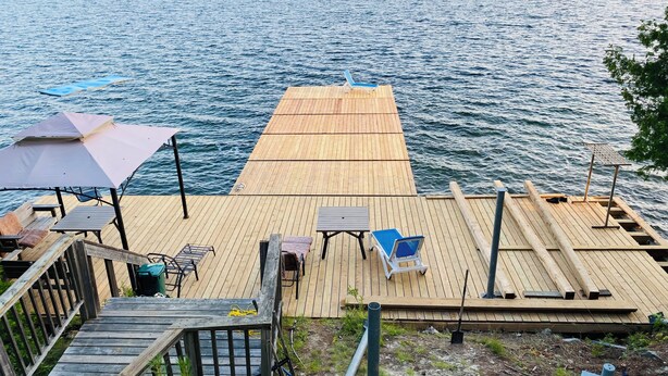 A wooden dock extending into a lake with a table and chairs, a covered area, and a staircase leading down. - Tamar Vacations (Temagami)