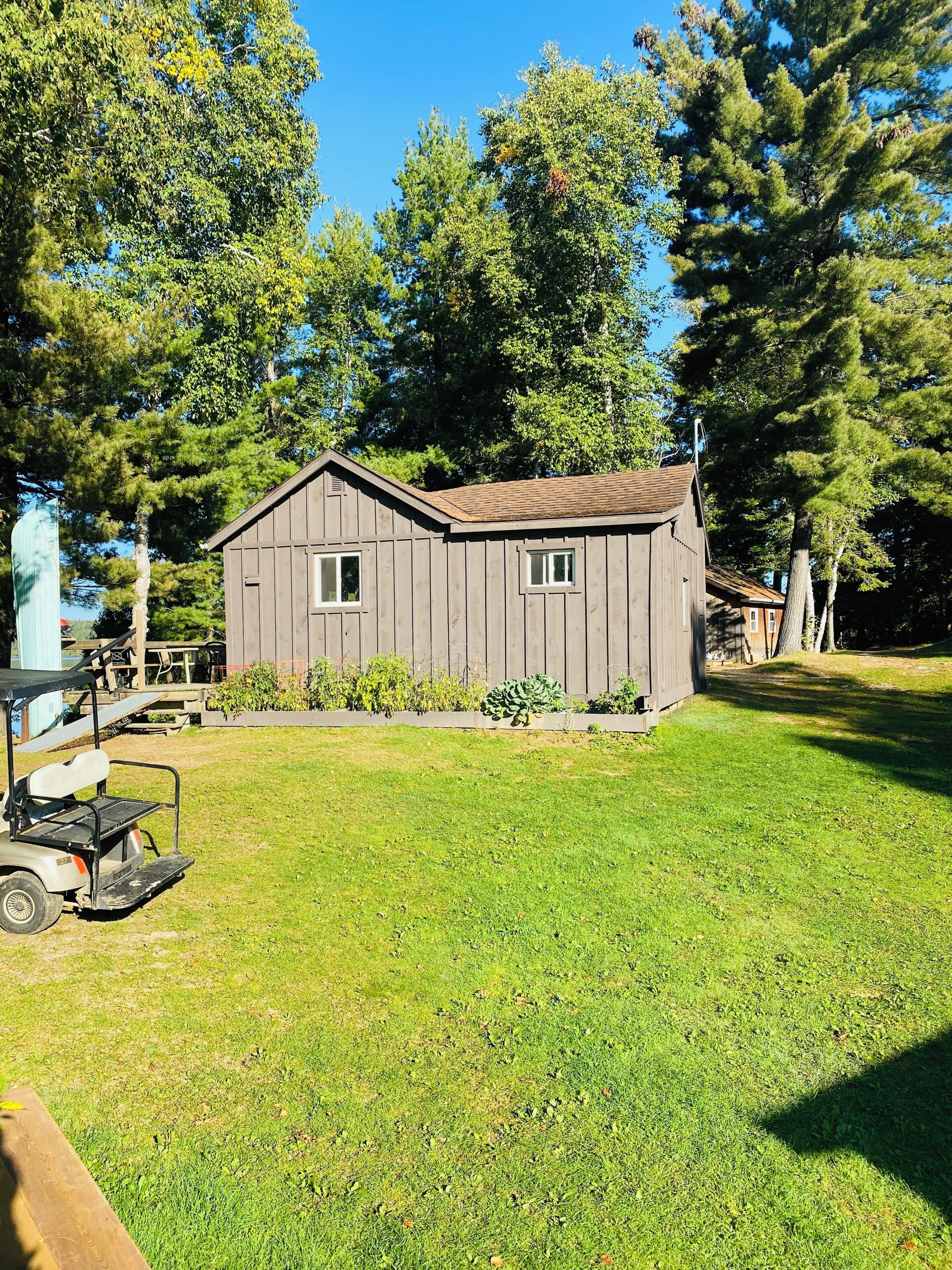A small wooden cabin with a sloped roof, surrounded by a well-maintained lawn and tall trees.