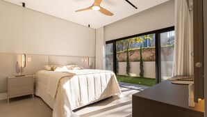 A modern bedroom with a bed, bedside table, and a view of a garden through a sliding door. - Mansão de Luxo a 35 minutos de SP (Araçariguama)
