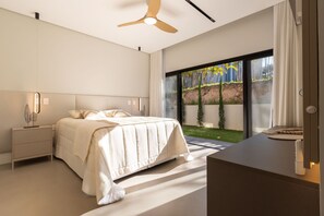 A modern bedroom with a bed, bedside table, and a view of a garden through a sliding door. - Mansão de Luxo a 35 minutos de SP (Araçariguama)