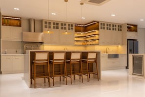 A modern kitchen with a central island, bar stools, recessed lighting, and built-in cabinetry. - Mansão de Luxo a 35 minutos de SP (Araçariguama)