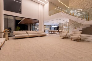 A spacious living area with a large beige sofa, two armchairs, a dining table, and a staircase with a unique design. - Mansão de Luxo a 35 minutos de SP (Araçariguama)