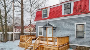 A house with a red roof, grey siding, and a wooden deck with stairs leading to a white door.