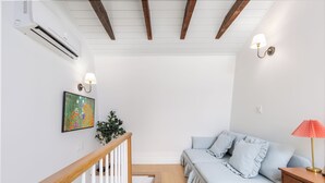 A bedroom with a bed, bedside table, lamp, and a wall-mounted air conditioner.