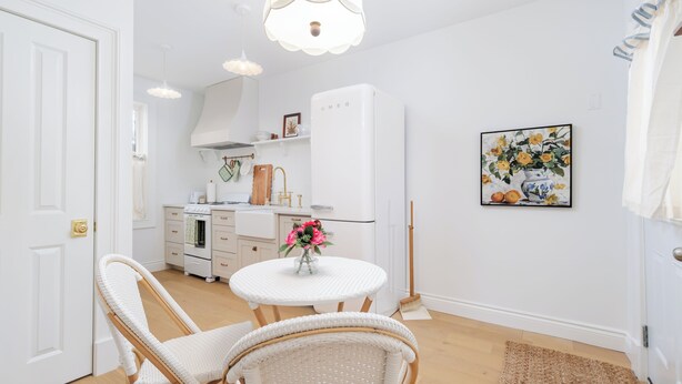 A compact kitchen with white appliances, a dining area with wicker chairs, and a small round table.