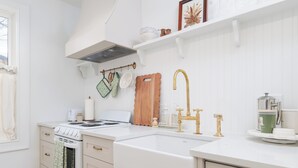A kitchen with white cabinetry, a white stove, a gold faucet, and a white countertop.