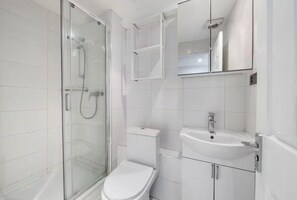 A modern bathroom with a glass-enclosed shower, a white toilet, and a sink with a mirror above it. - Liverpool Street Station - Stylish Apartment (London)