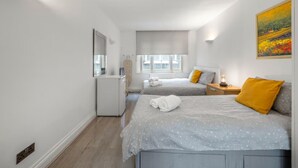 Ein Schlafzimmer mit zwei Betten, einem Schminktisch, einem Fenster mit Jalousien und einem Bild an der Wand.