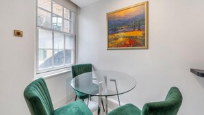 Ein Zimmer mit einem Glastisch, grünen Stühlen, einem Gemälde und einem Fenster.