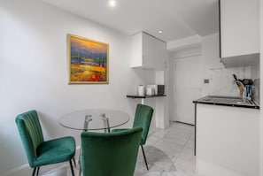 A modern kitchen with a dining area, a painting on the wall, and a small table with chairs. - Liverpool Street Station - Stylish Apartment (London)
