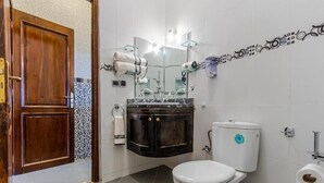 A bathroom with a wooden door, a white toilet, a black vanity, a mirror, and a towel rack. - Le joyau de l'ourika (Ourika)