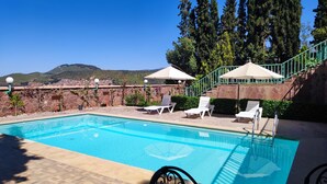 A swimming pool with lounge chairs and umbrellas, surrounded by stone walls and greenery, with a view of distant hills. - Le joyau de l'ourika (Ourika)