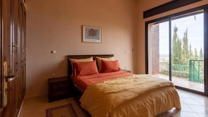 A bedroom with a bed, a nightstand, a dresser, a window with a view, and a wall-mounted artwork. - Le joyau de l'ourika (Ourika)