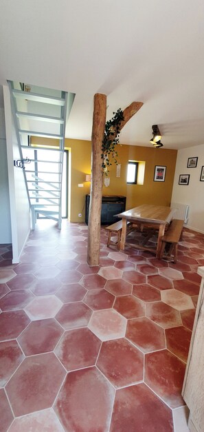 Ein Zimmer mit sechseckigem Fliesenspiegel, einem Holztisch mit Bänken, einer Treppe und einem Deckenventilator.