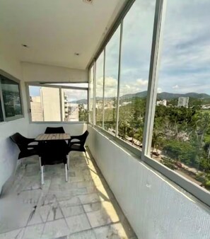 A balcony with a table and chairs, large windows, and a view of buildings and greenery. - Acapulco Costera, Zona Dorada 300 m from the sea 🏖️🌊 (ACAPULCO DE JUÁREZ)