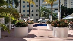 En hotelgård med palmer, plantekasser med blomster og en swimmingpool.