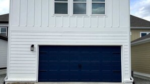 Uma casa de dois andares com porta de garagem, varanda pequena e céu claro.