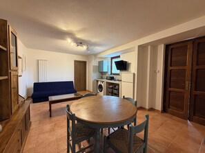 Un espacio habitable compacto con una mesa de comedor, sillas, un sofá, lavadora, televisor y puertas de madera.