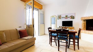 A living room with a sofa, a dining table with chairs, a television, and a fireplace. - Casetta sulla spiaggia by Casa di Marco (Padula Bianca)