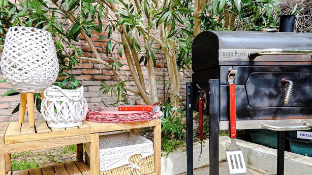 A barbecue grill, wicker baskets, and a wooden table with a brick wall in the background. - Casetta sulla spiaggia by Casa di Marco (Padula Bianca)