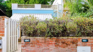 A brick wall with a metal gate, a blue roof, and a staircase leading to a balcony. - Casetta sulla spiaggia by Casa di Marco (Padula Bianca)