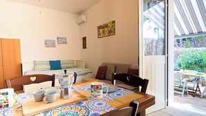 A dining area with a table set for two, a sofa, and a bed in the background. - Casetta sulla spiaggia by Casa di Marco (Padula Bianca)
