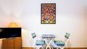 Una stanza piccola con TV, un tavolo, due sedie e un quadro astratto e colorato appeso al muro.